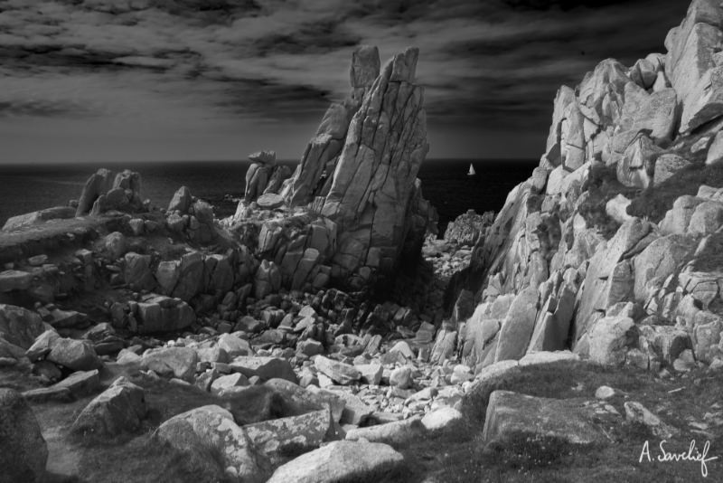 Voilier passant au loin, aperçu dans une percée entre les rochers sur la côte de Bretagne