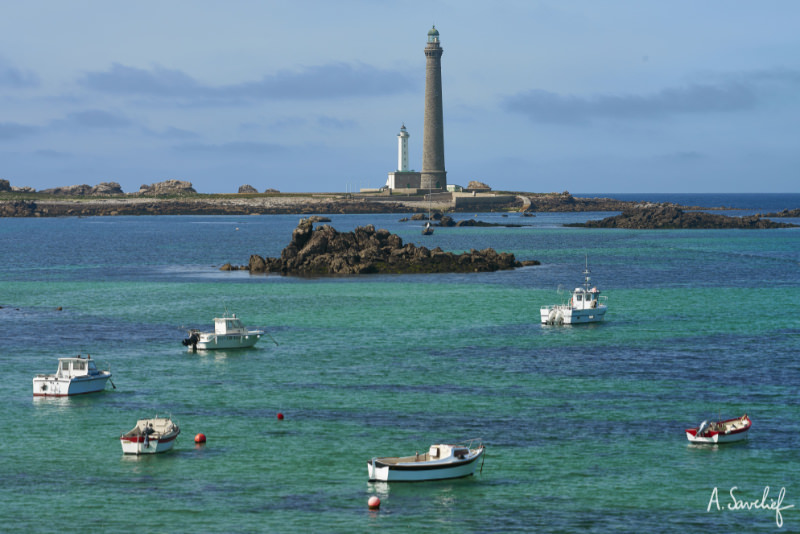 Bateaux de pêcheurs et découpes de rochers devant les deux phares de l’Île Vierge père et fils, sur la côte de Bretagne